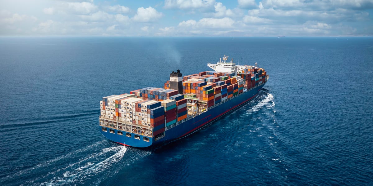 A large container cargo ship travels over calm, blue ocean