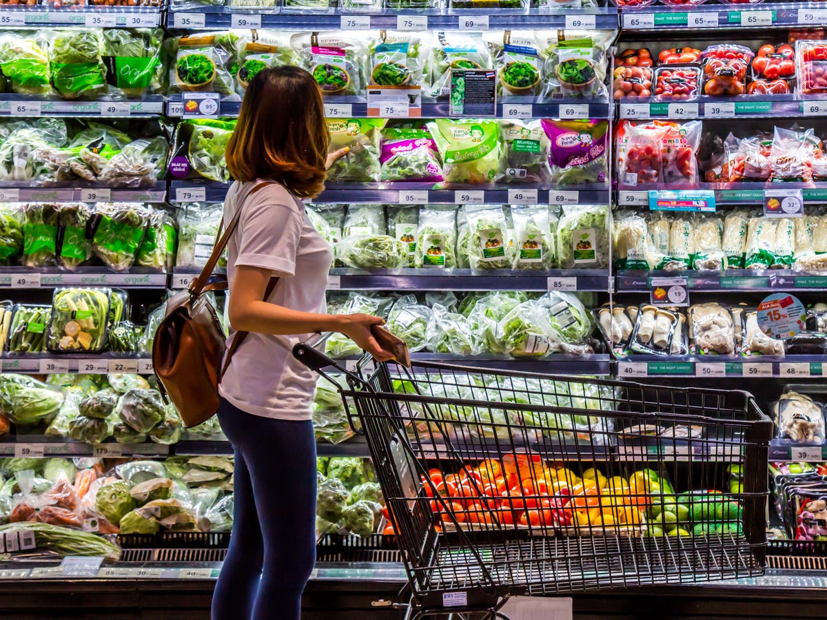 Woman holding push cart along supermarket chiller aisle