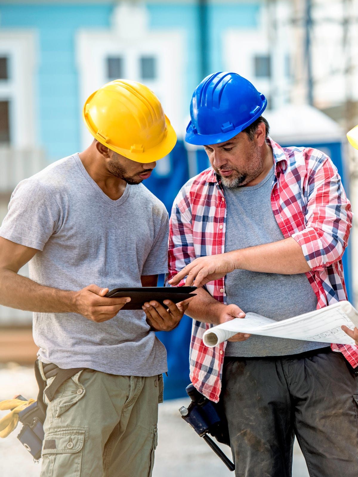 Three men wearing hard hat, holding blueprint and tablet