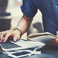 Man typing while holding a notebook