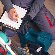 Top shot of man writing on the a checklist beside refrigerant tank and pressure gauge