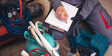 Top shot of man writing on the a checklist beside refrigerant tank and pressure gauge