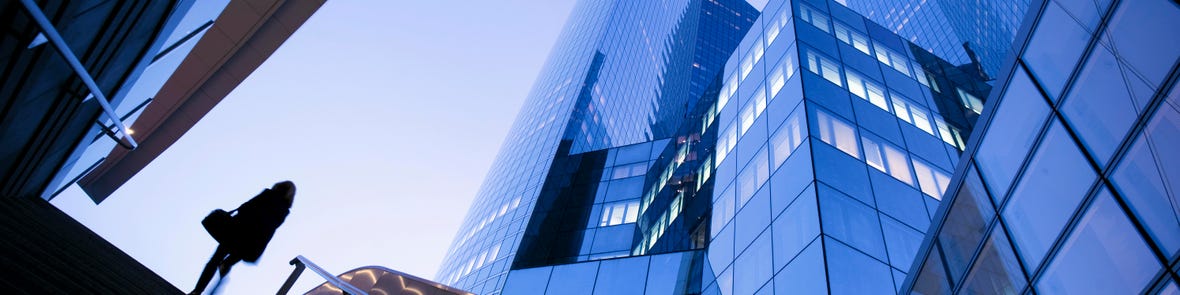 Silhouette of a person walking up stairs beneath towering modern skyscrapers at dusk.