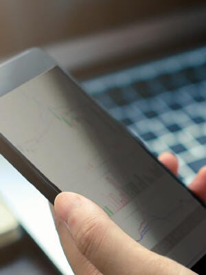 Man holding a mobile phone with blurry laptop keyboard background