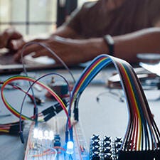 Electronic wires and microcontroller, blurry man typing in the background