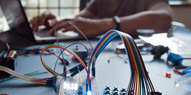 Electronic wires and microcontroller, blurry man typing in the background