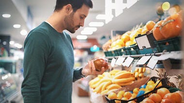 Man holding an apple by the supermarket chiller aisle