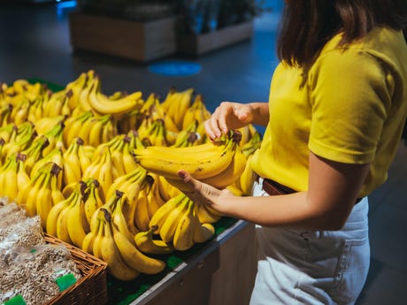 woman taking yellow bananas from the store shelf grocery shopping concept